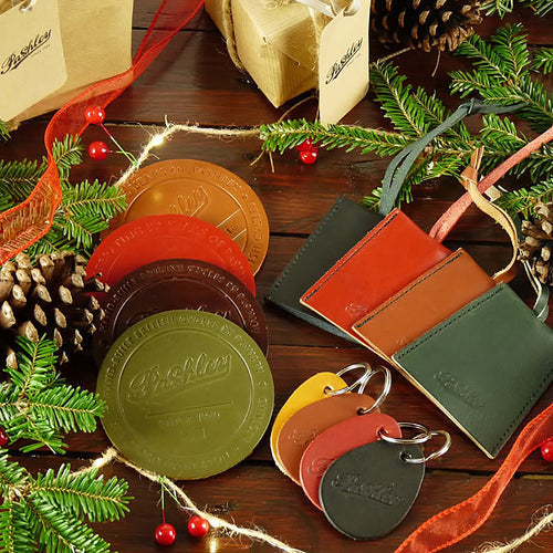 Selection of colourful leather Pashley circular coasters and key rings, surrounded by Christmas foliage.