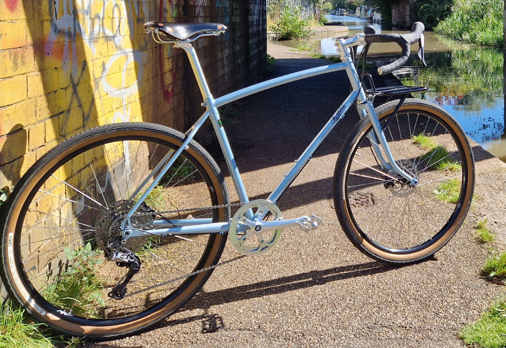 Light blue retro bicycle with drop handlebars and black leather saddle parked by a canal with graffiti visible on the adjacent wall