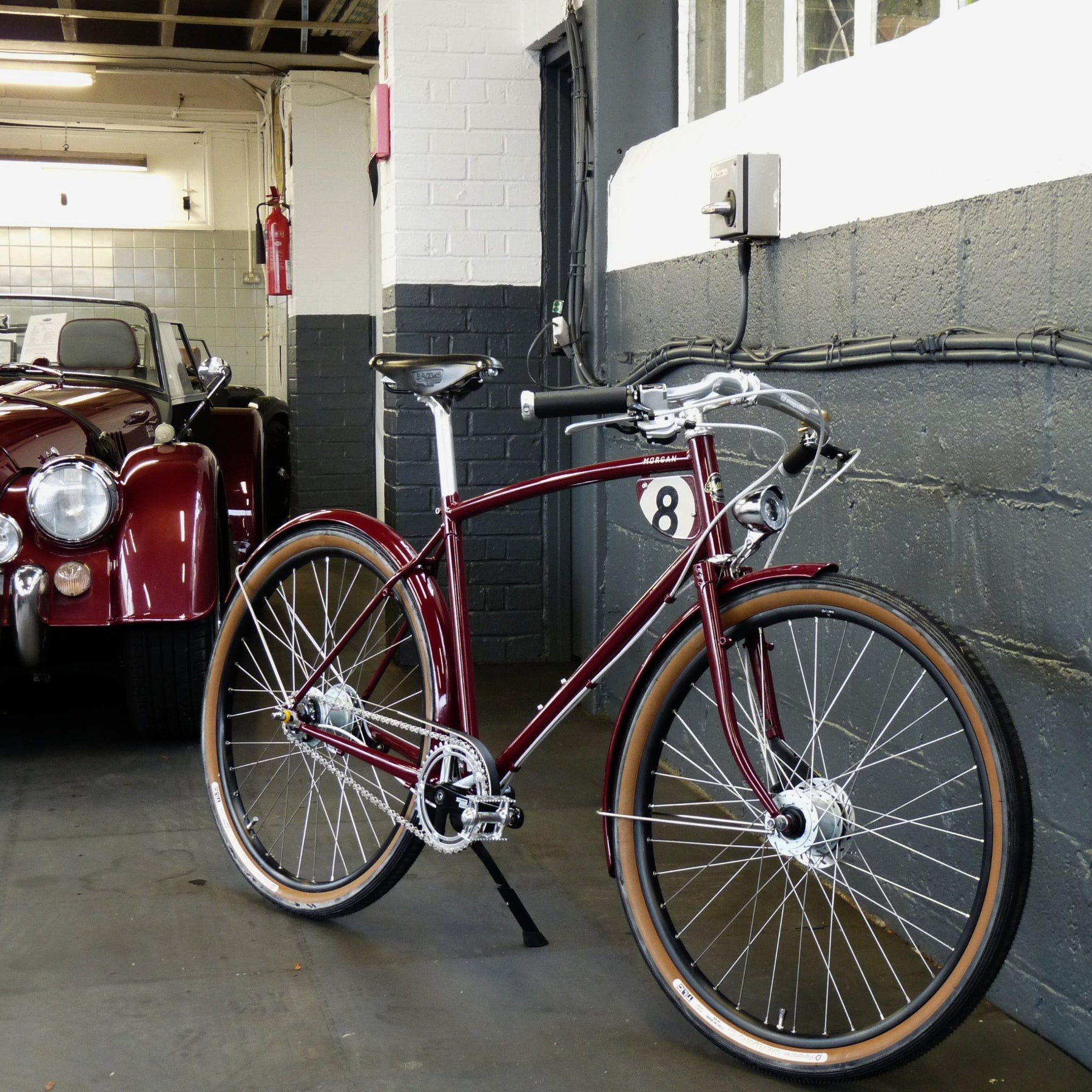 a burgundy Morgan 8 bicycle next to a morgan car