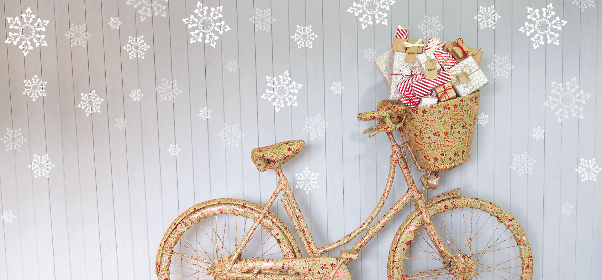 A Pashley bicycle wrapped in Christmas wrapping paper, with Christmas presents in its basket.